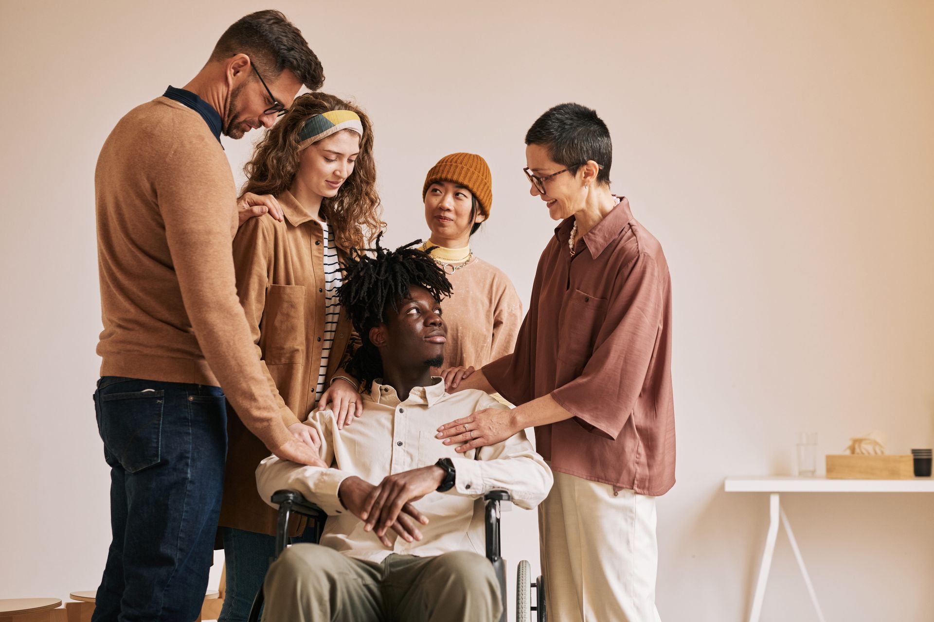 Small group gathered around a seated person, discussing something in a bright room with a white table.
