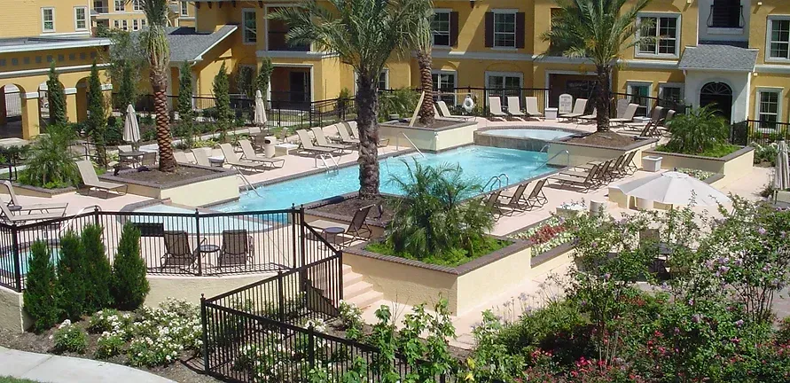A large swimming pool surrounded by chairs and umbrellas in front of a building