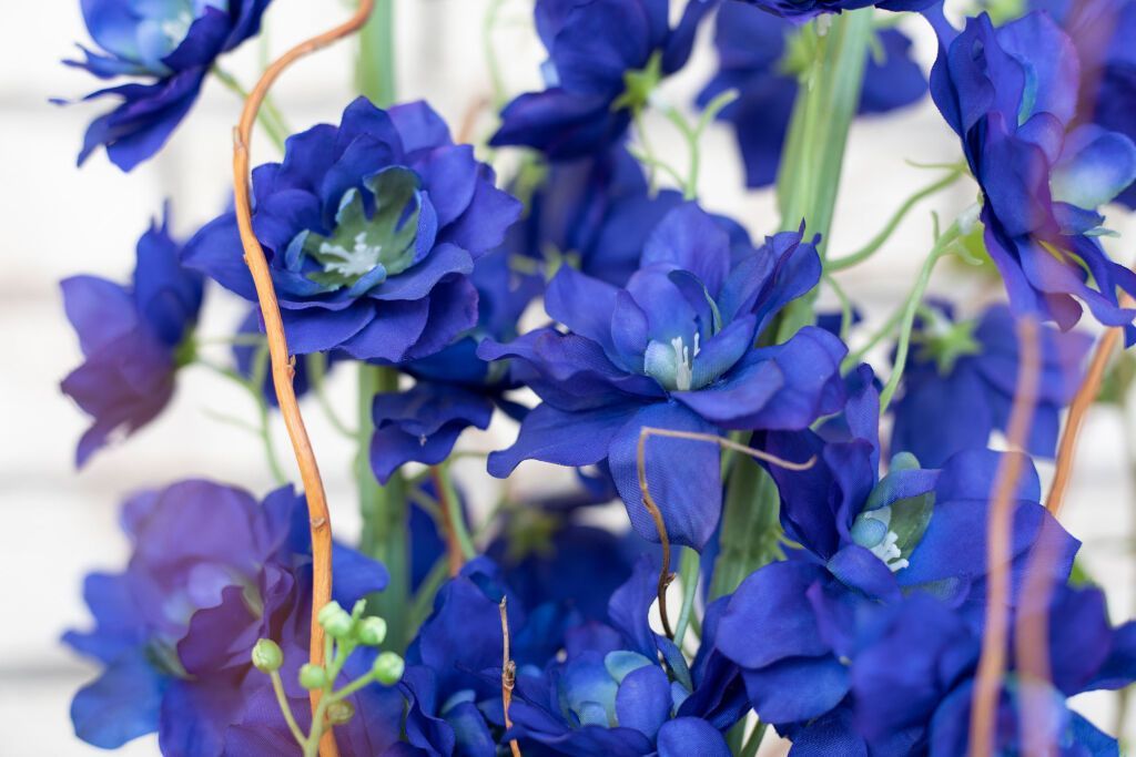 Blue artificial flowers, close-up. Features a bundle of dark blue flowers with green stems and brown twigs.