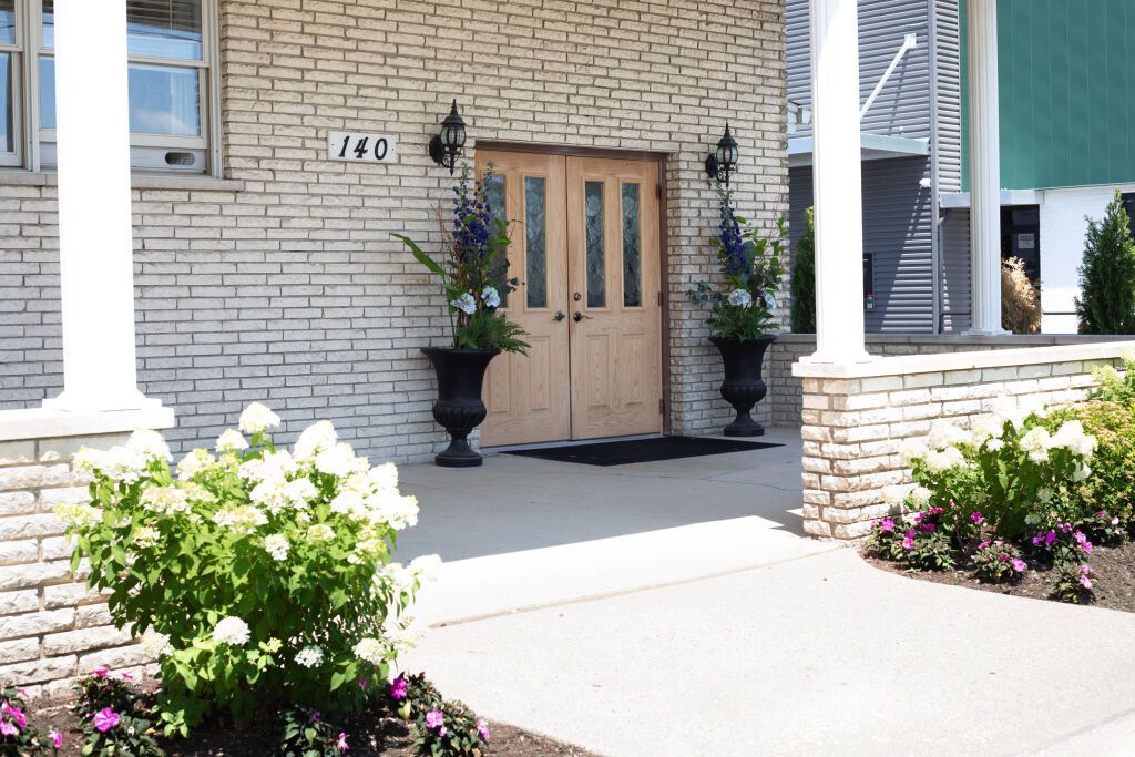 Building entrance with beige brick, wooden doors, and potted flowers.