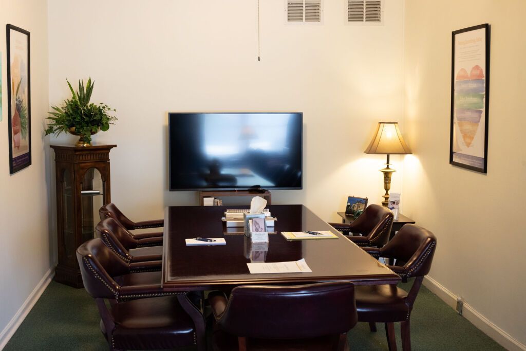 A conference room with a large screen, table, chairs, lamp, and two framed posters on the walls.