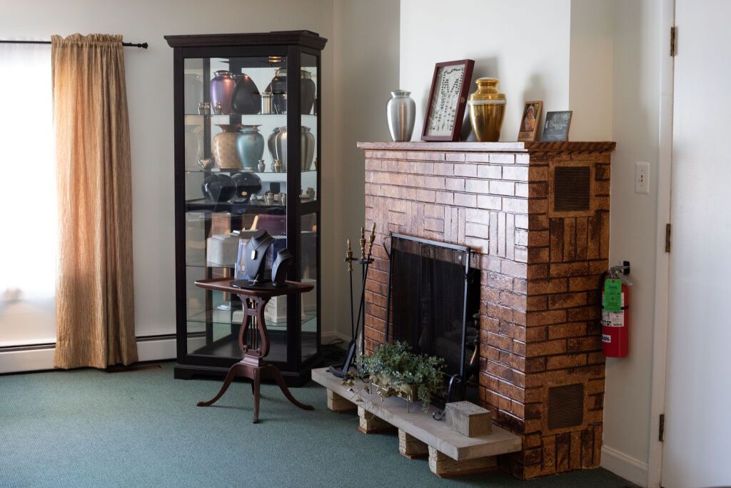 Fireplace and display cabinet in a living room; brown brick, green carpet, gold curtains.
