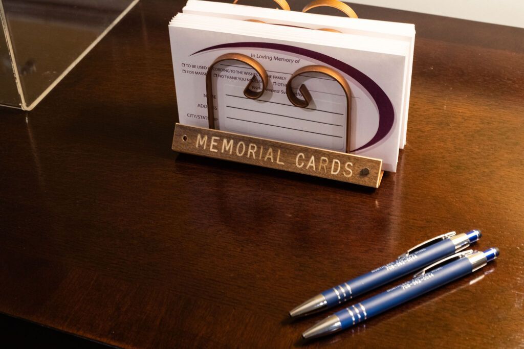 Memorial cards and pens on a brown surface. A holder reads 
