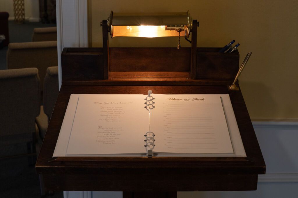 Wooden desk with illuminated lamp, open book, and pens, likely for guest signing.