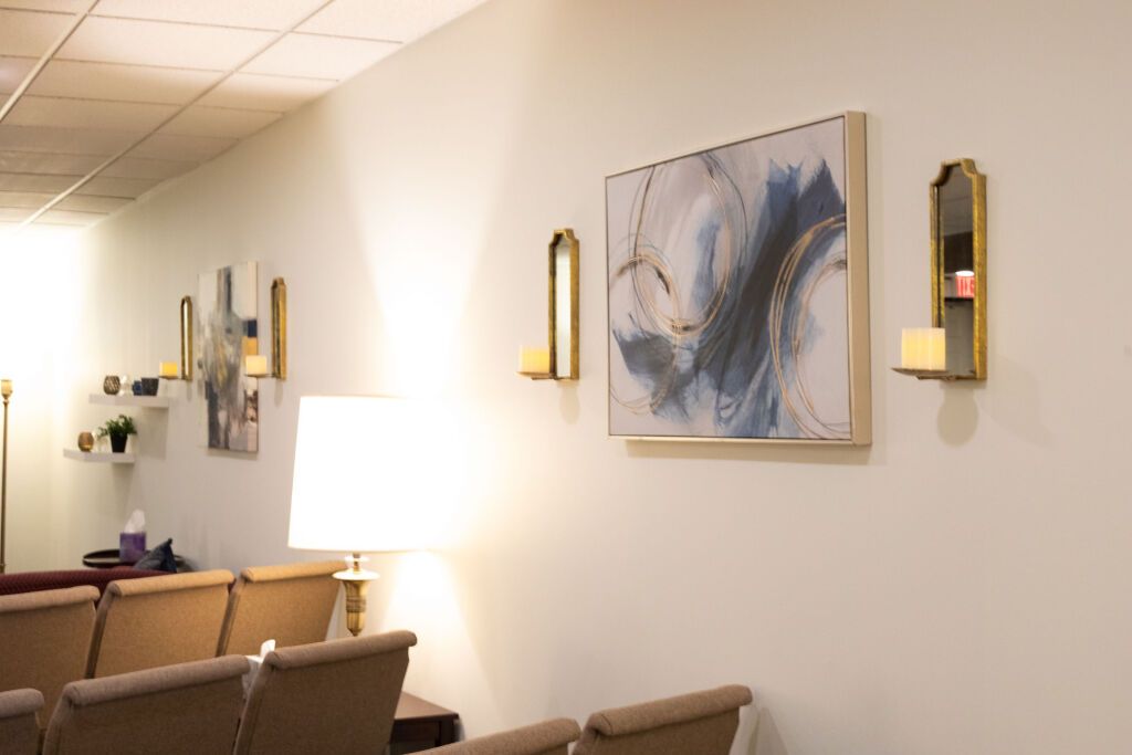 A room with chairs, art, wall sconces, and a lit lamp against a white wall.