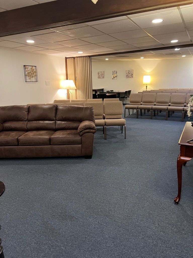 A large room with blue carpet, brown sofa, chairs, tables, and lamps, with a curtained doorway in the background.