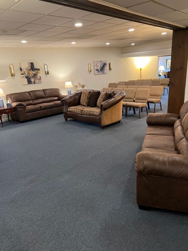A waiting room with brown couches, chairs, and art on the walls. The floor is covered in blue carpet.