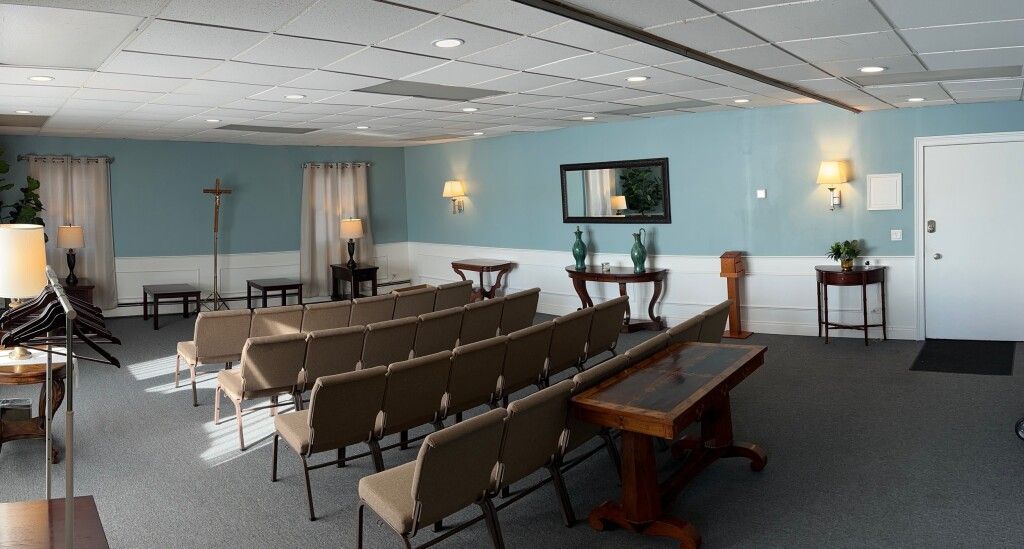 A funeral home chapel with rows of beige chairs, a wooden podium, and blue walls.
