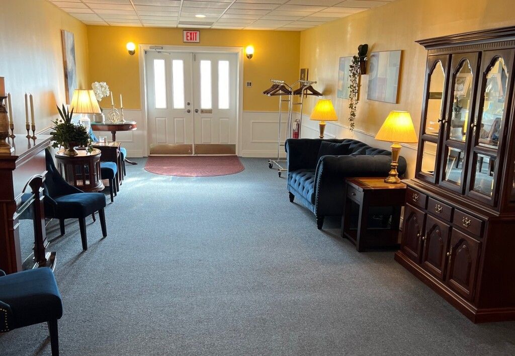 Interior of a room with chairs, a couch, lamps, and a wooden cabinet; a door is at the end.