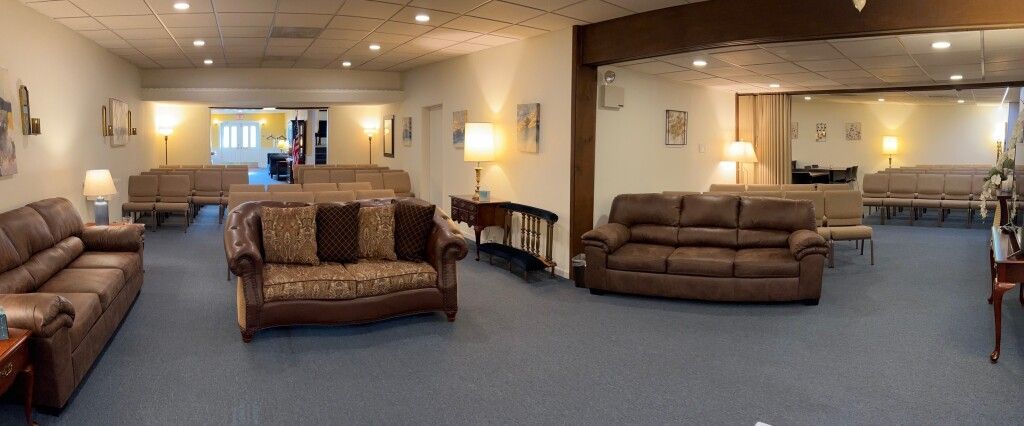 A waiting room with multiple brown couches, lamps, and a blue carpet.