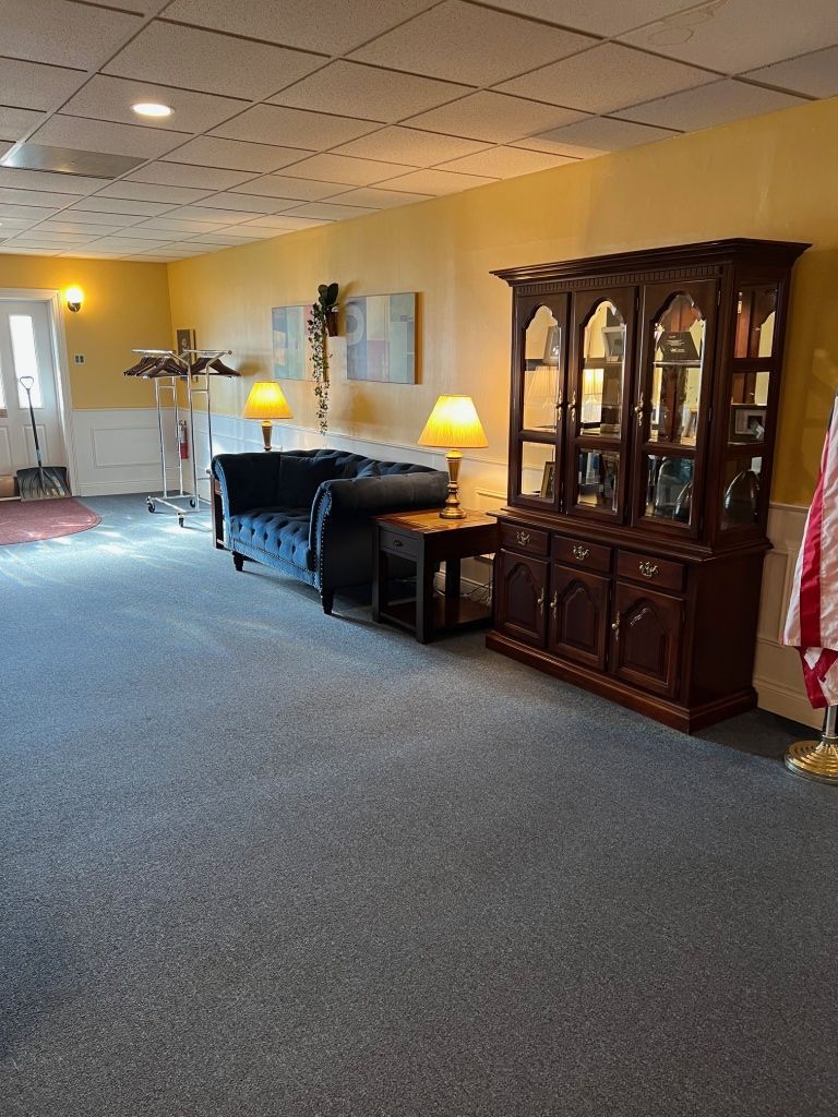 A waiting room with blue couch, dark wooden cabinet, lamps, and a door, carpeted floors.
