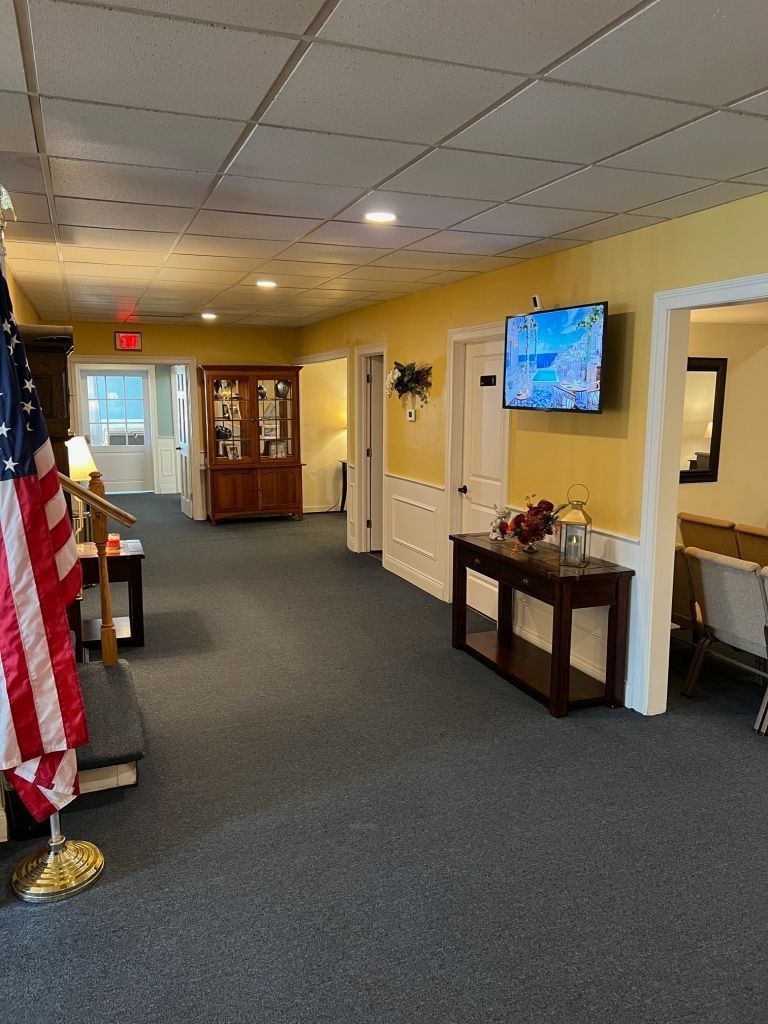 Hallway with yellow walls, dark carpet, American flag, television, and dark wood furniture.