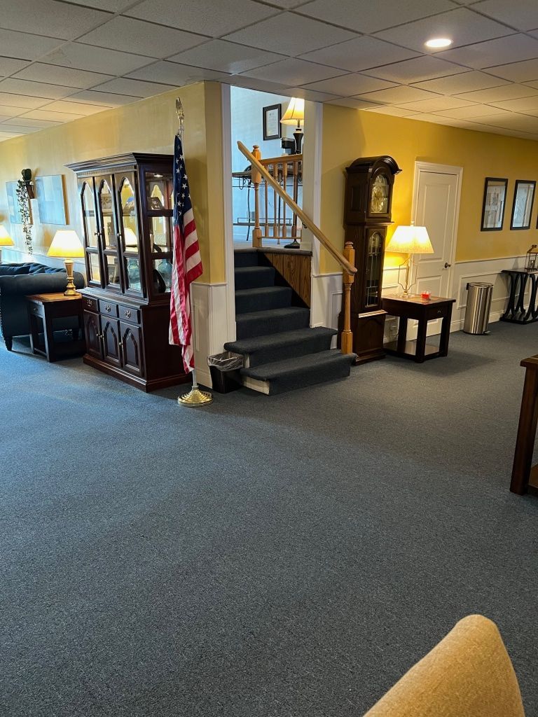 Interior with blue carpet, stairs, furniture, lamps, and an American flag.