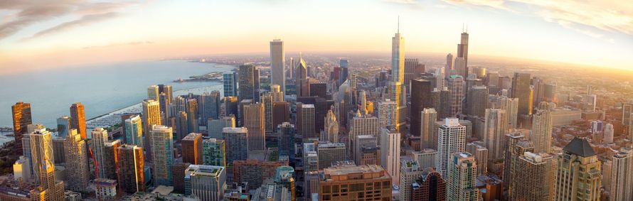 Aerial view of Chicago skyline at sunset, with buildings of various heights. The lake is visible on the left side.
