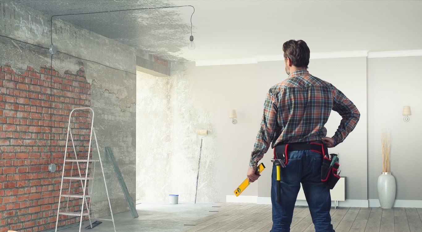 Worker holding a yellow power tool in a room under renovation, with exposed brick and dust