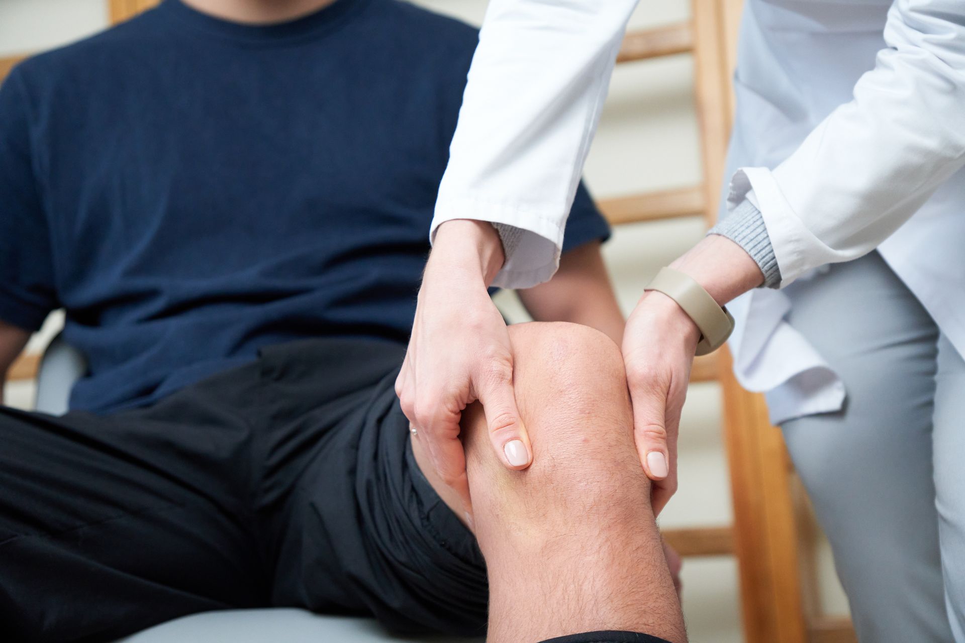 Ein Arzt untersucht das Knie eines Patienten in seiner Arztpraxis.