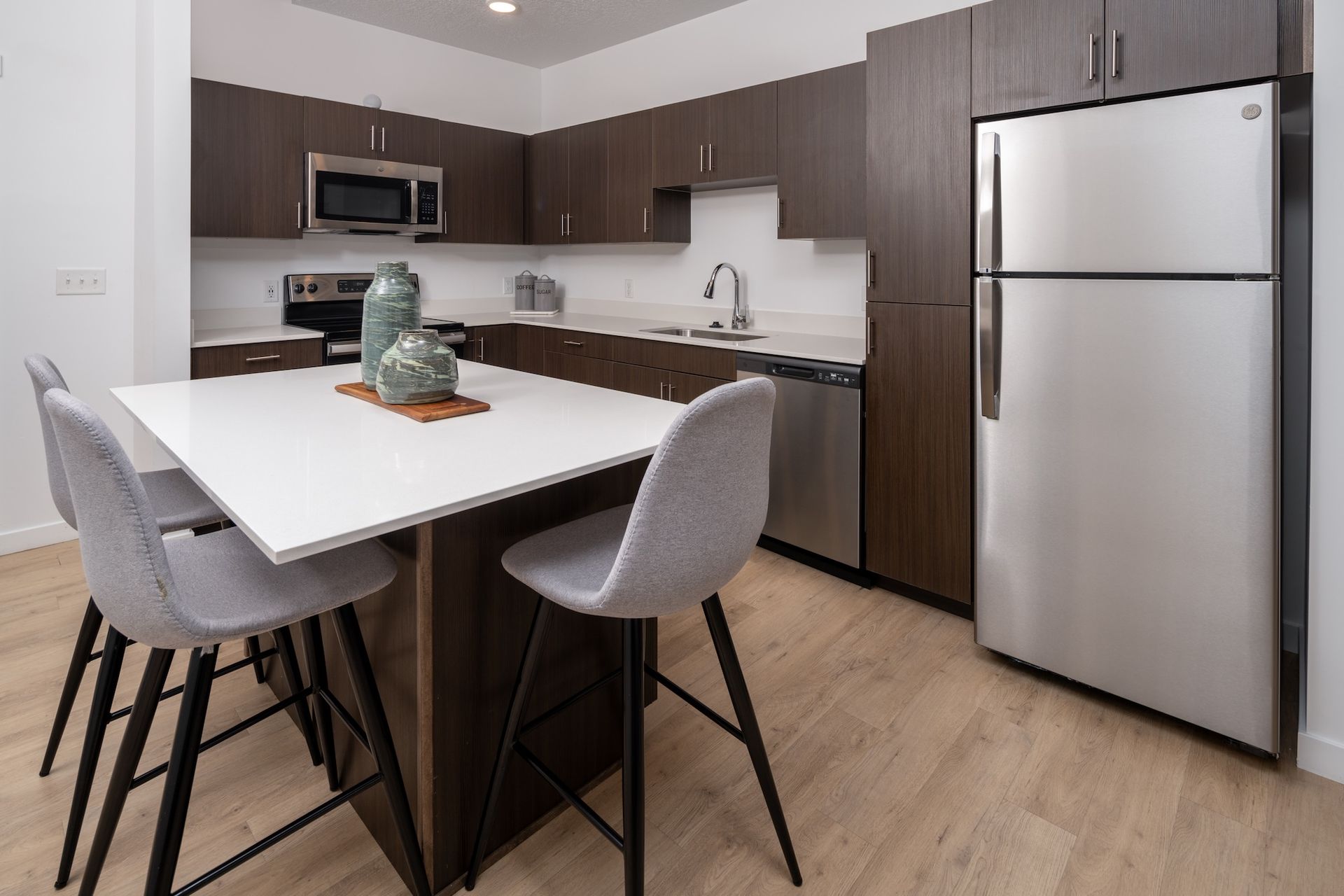 Modern kitchen with dark cabinets, white countertop island with chairs, stainless steel appliances.