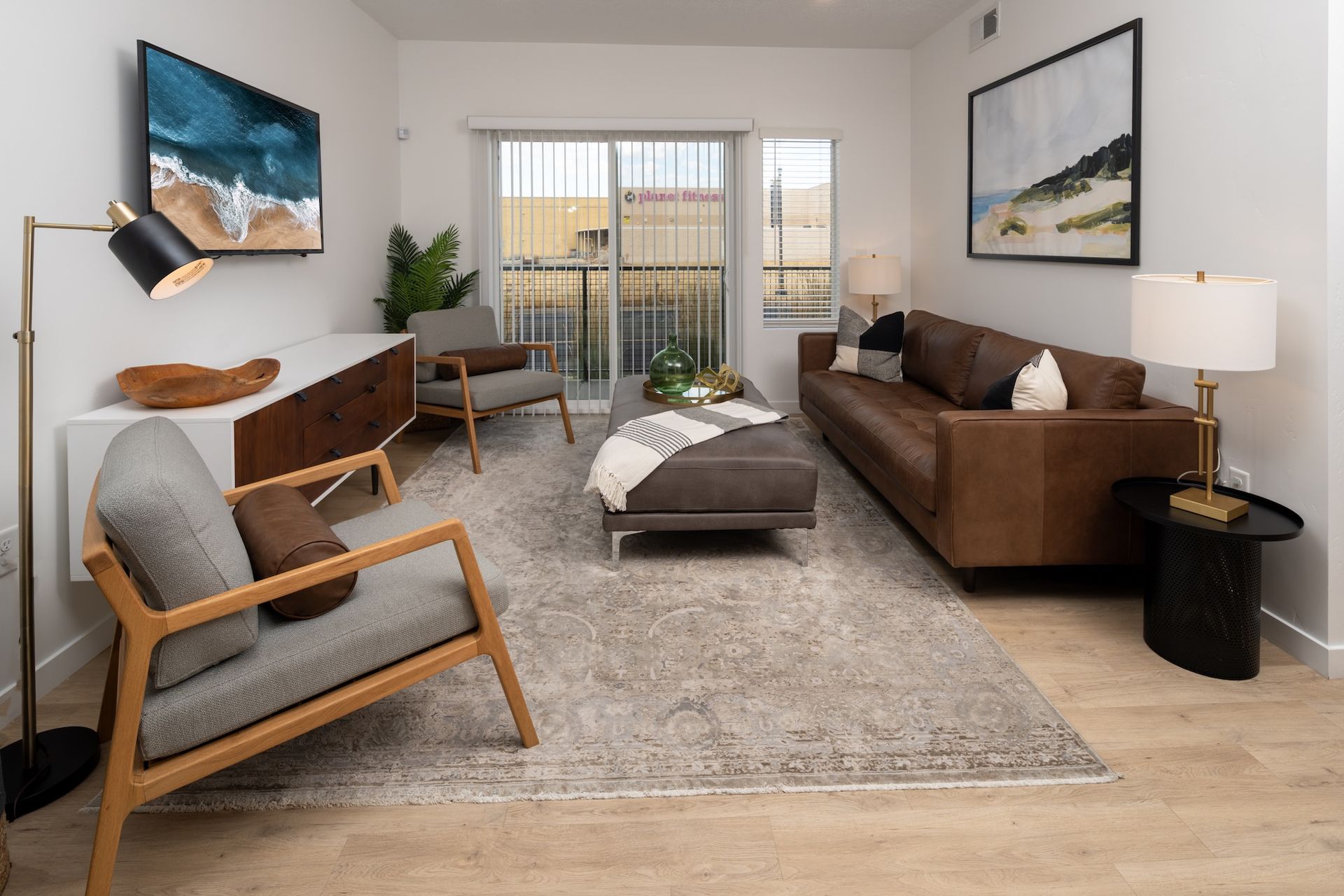 Living room with brown leather sofa, chairs, rug, and artwork.