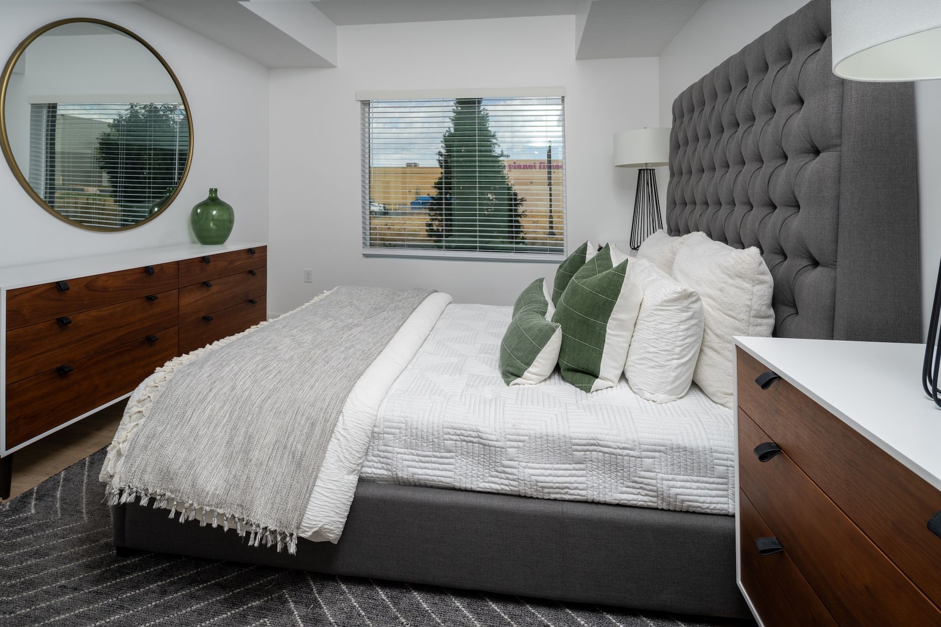 Bedroom with gray tufted headboard, white bedding, green pillows, and wooden dresser.