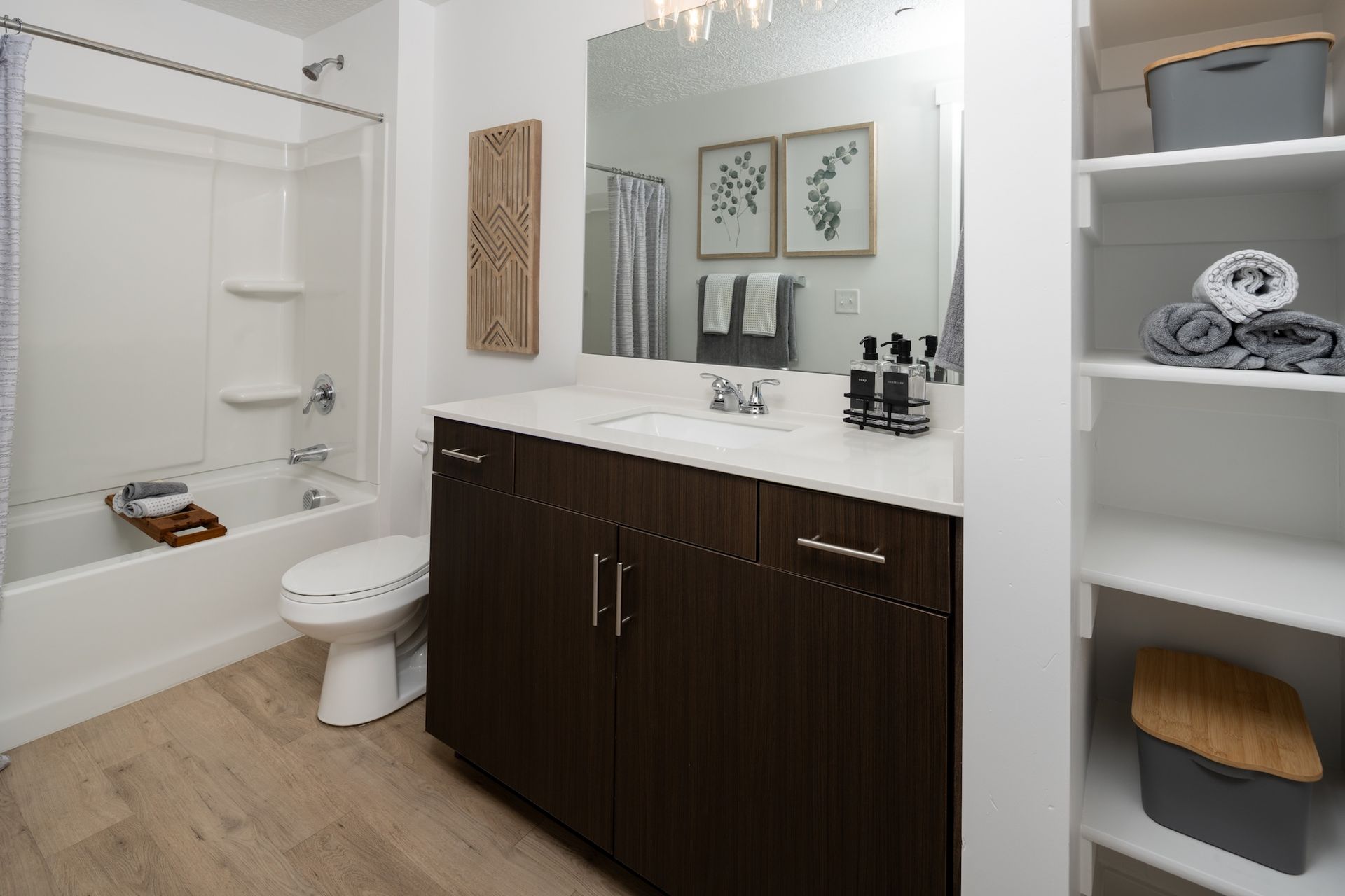 Bathroom with brown vanity, white countertop, shower/tub, and open shelving.