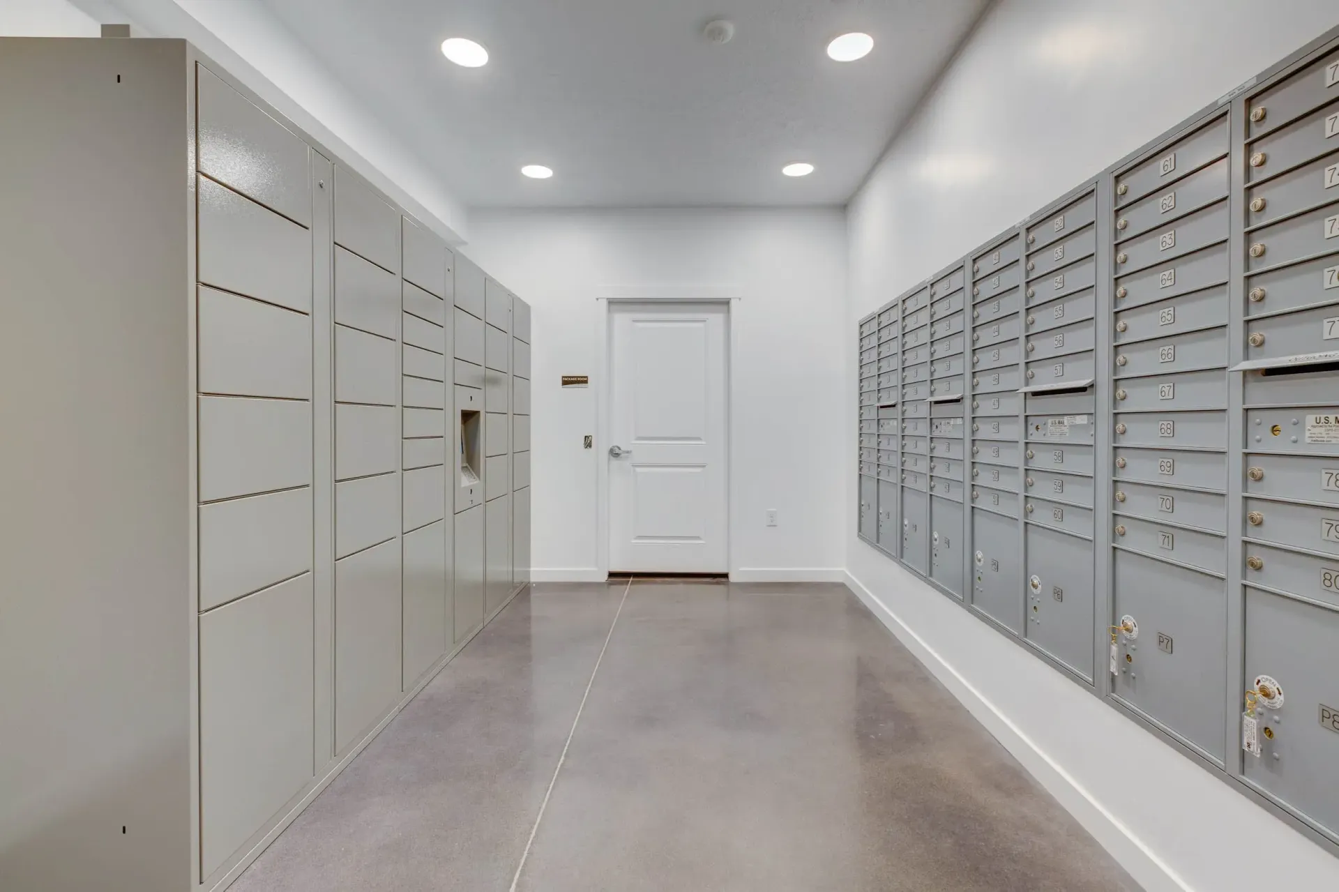 Mailroom hallway with gray mailboxes lining both walls, white door at the end.