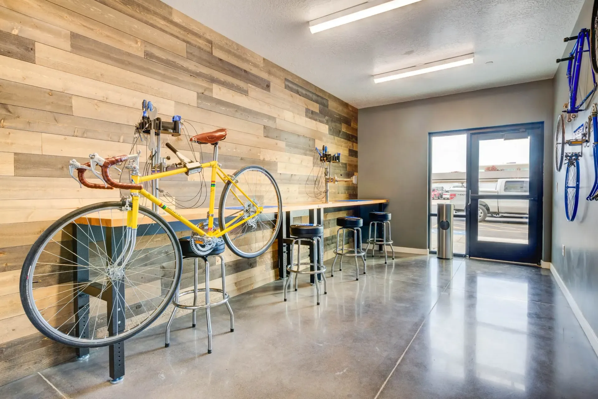 Bike repair shop with yellow bike on stand, wood panel wall, stools, door.