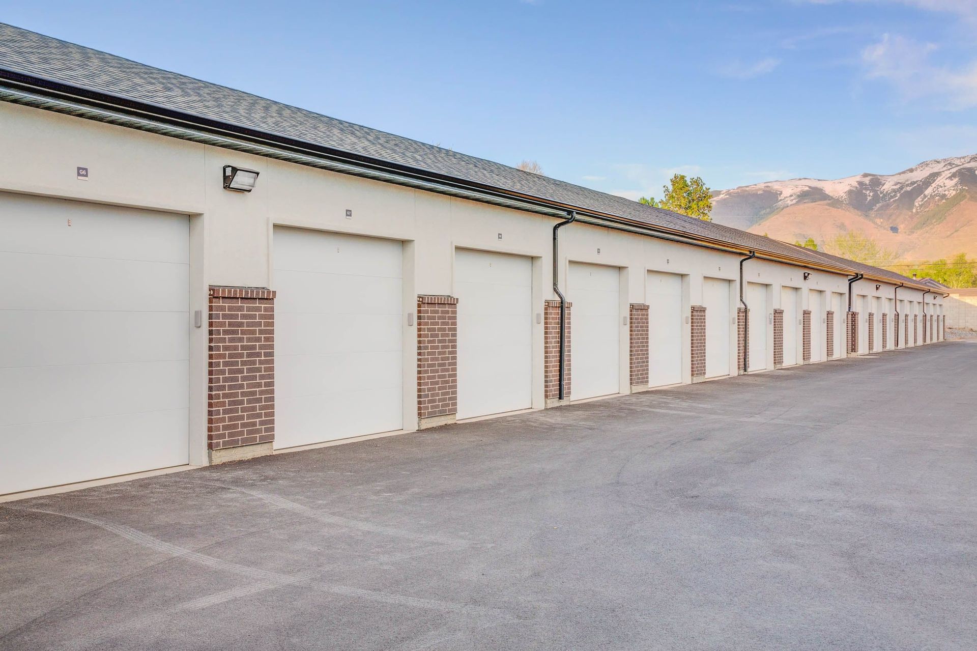 Storage units with white doors and brick accents under a blue sky and mountains.