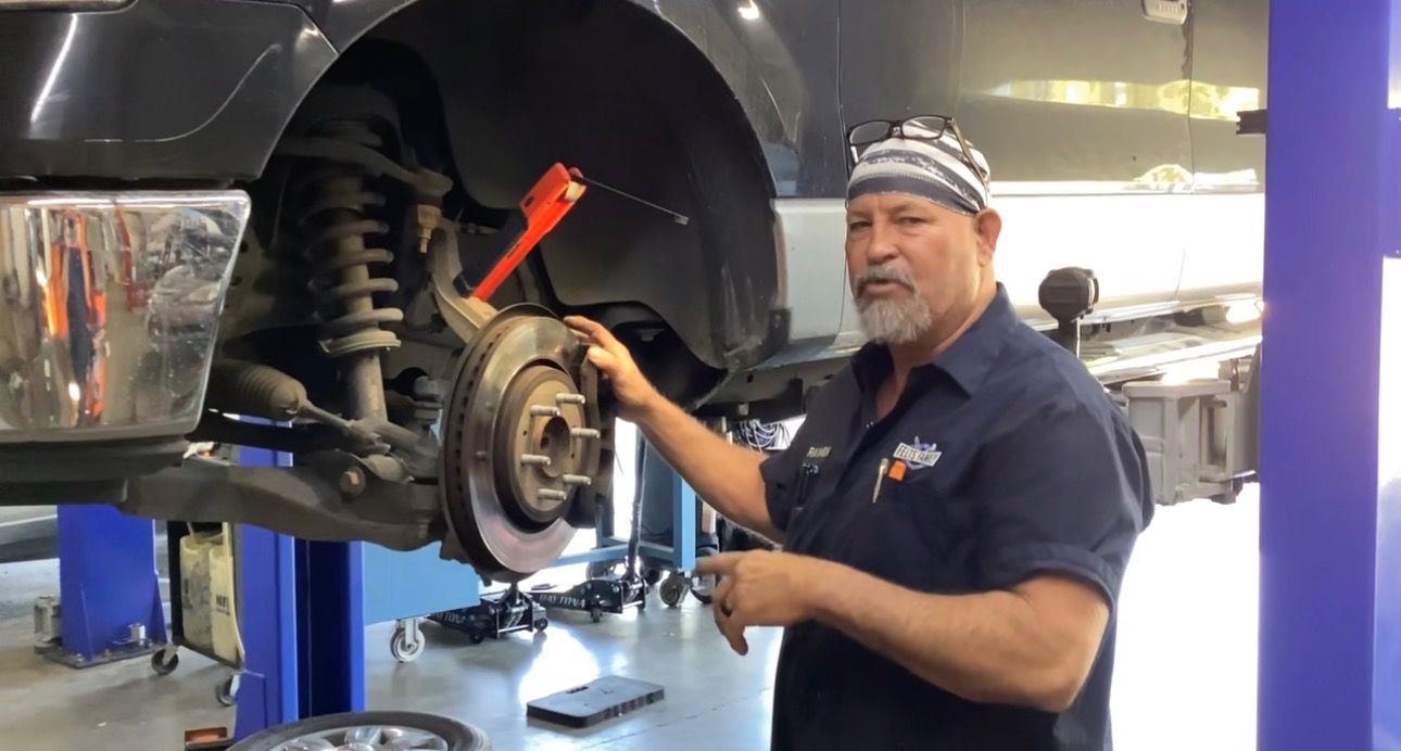 Mechanic working on a car’s exposed wheel and brake assembly in an auto shop