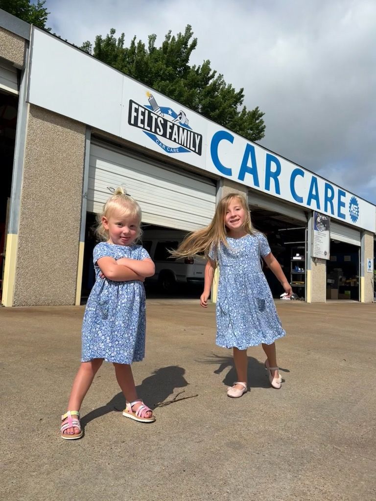 Two children in blue dresses standing outside a car care shop with a sign overhead.