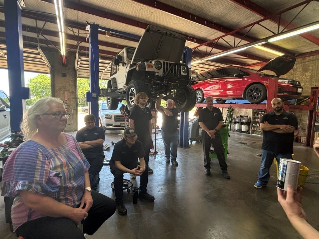 Classic car meet in a garage, with a raised black off-road vehicle and a red sports car in the background.