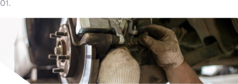Gloved mechanic working on a car brake rotor and suspension assembly in a garage