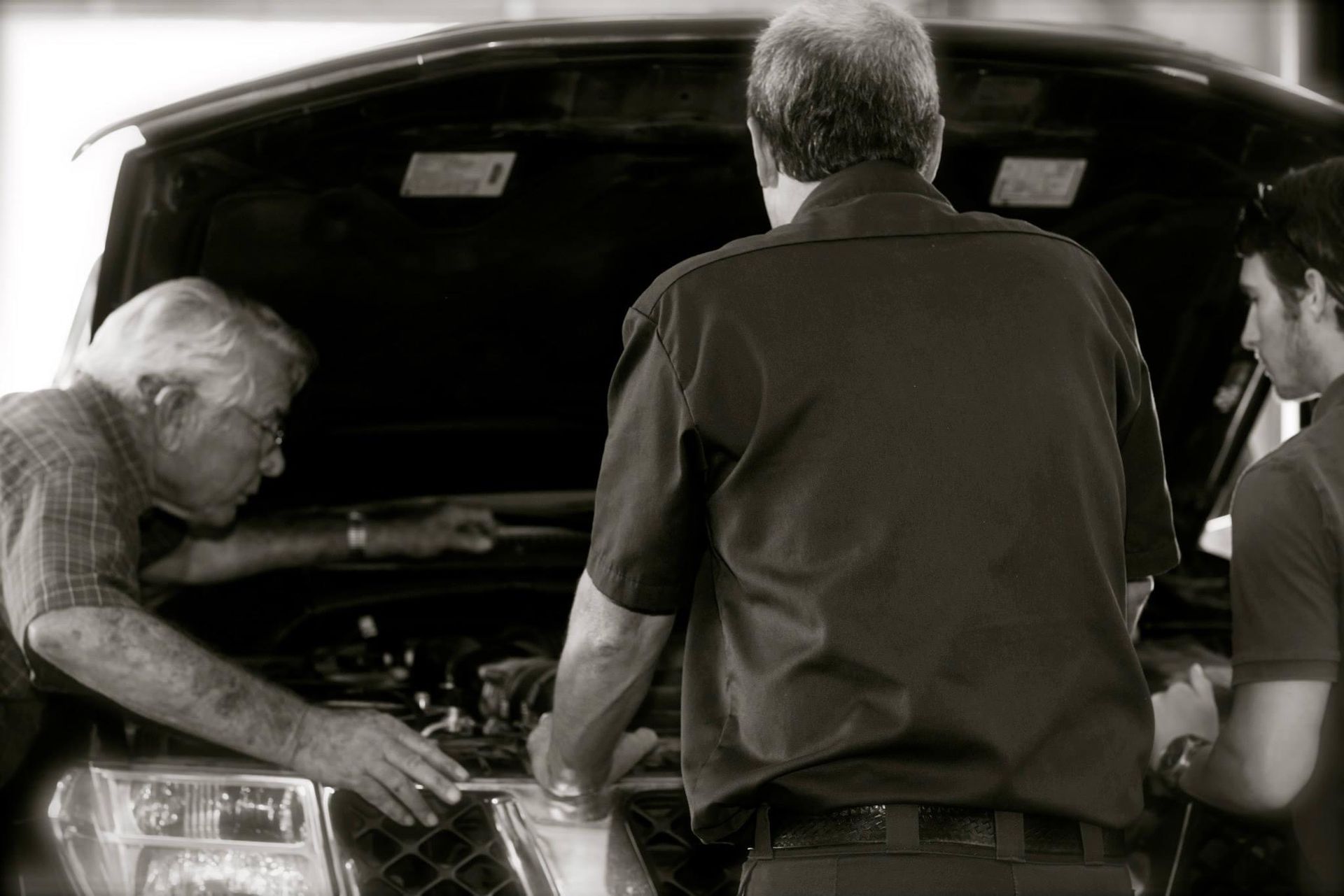 Three people inspecting the engine of a car with its hood open