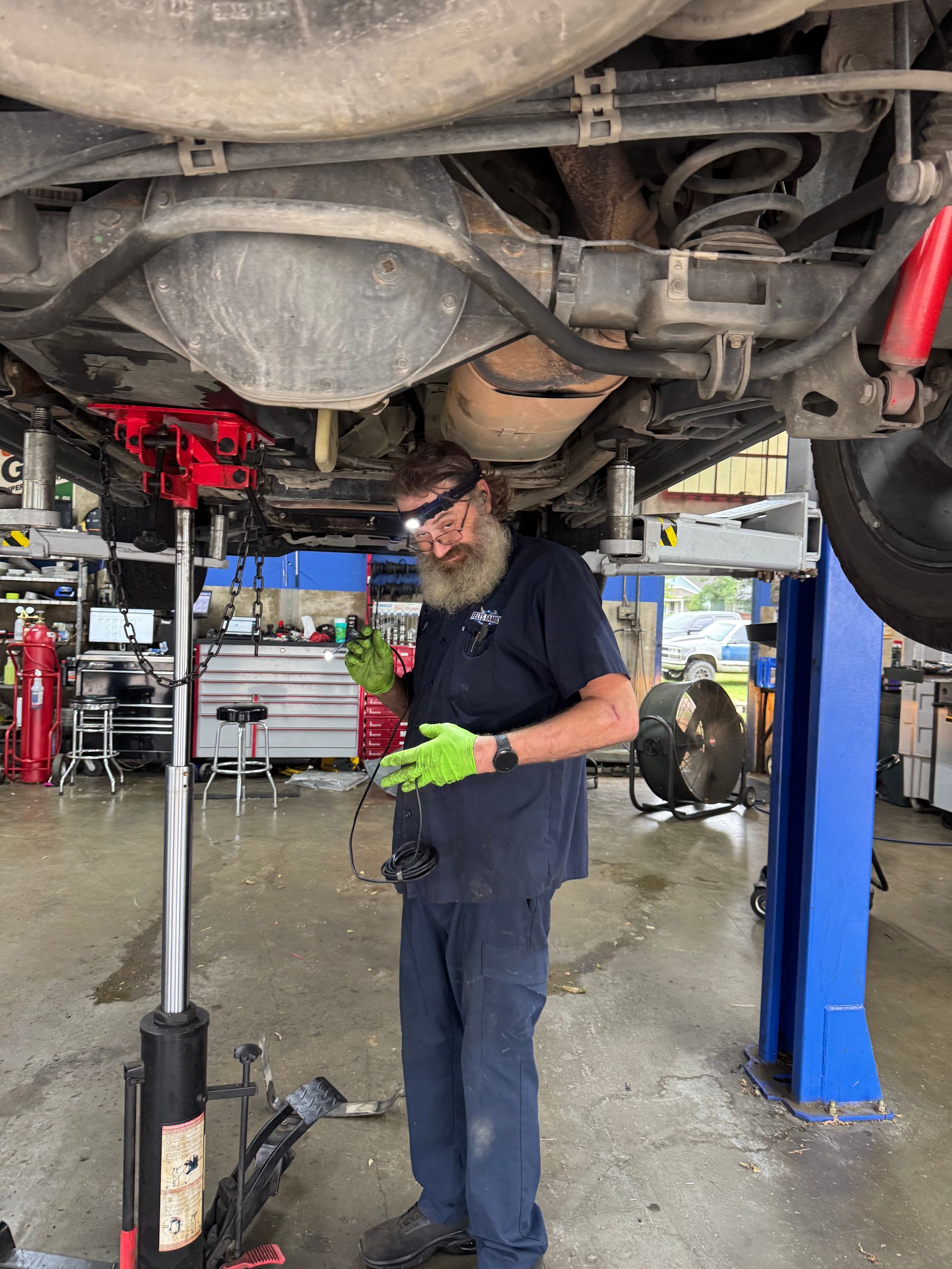 Mechanic under a lifted vehicle using a tool in a shop bay