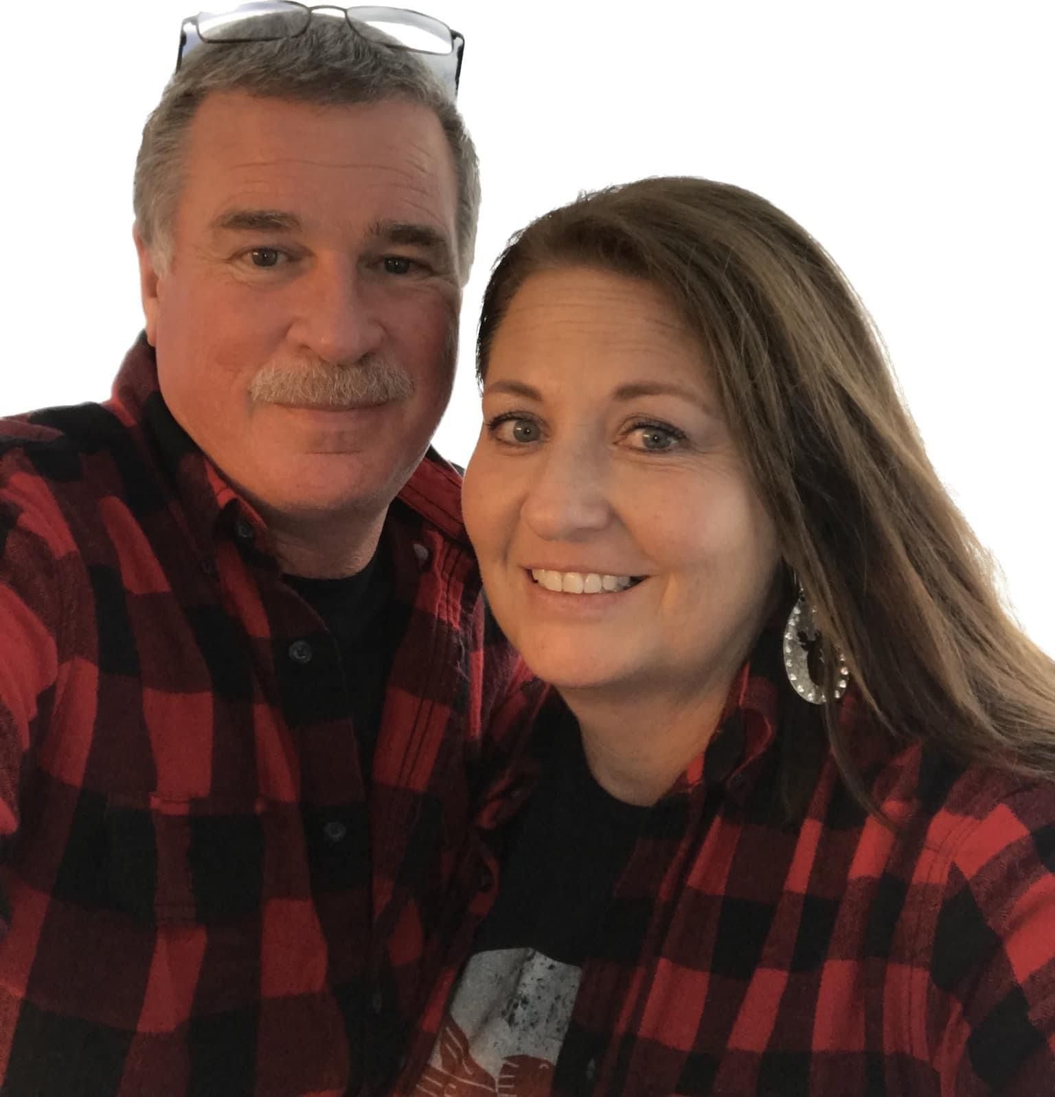 Two people in matching red plaid shirts smiling at the camera against a white background