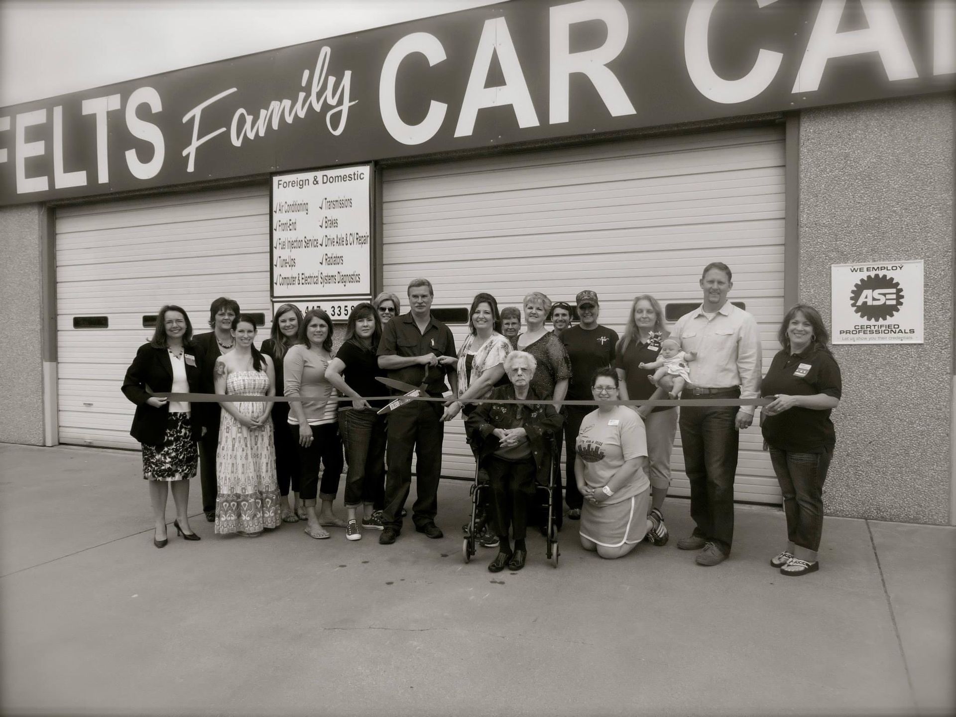 Group of people posing outside a car dealership with a large “CAR” sign and storefront behind them.