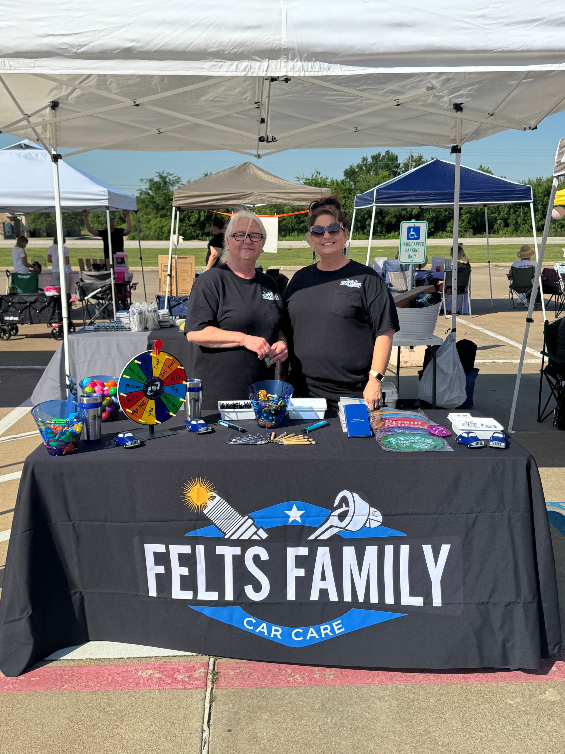 Two people behind a FELTS Family Care Care booth under a white canopy, with colorful items on the table.