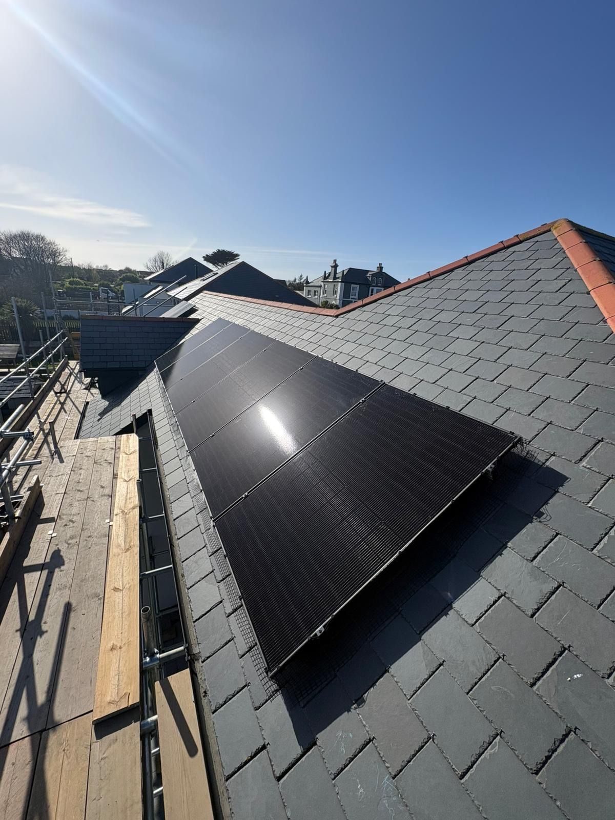 Solar panels on a house roof with an electric vehicle charging station in front, surrounded by greenery.