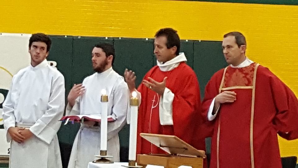 priest and alte boys at a mass in the gym