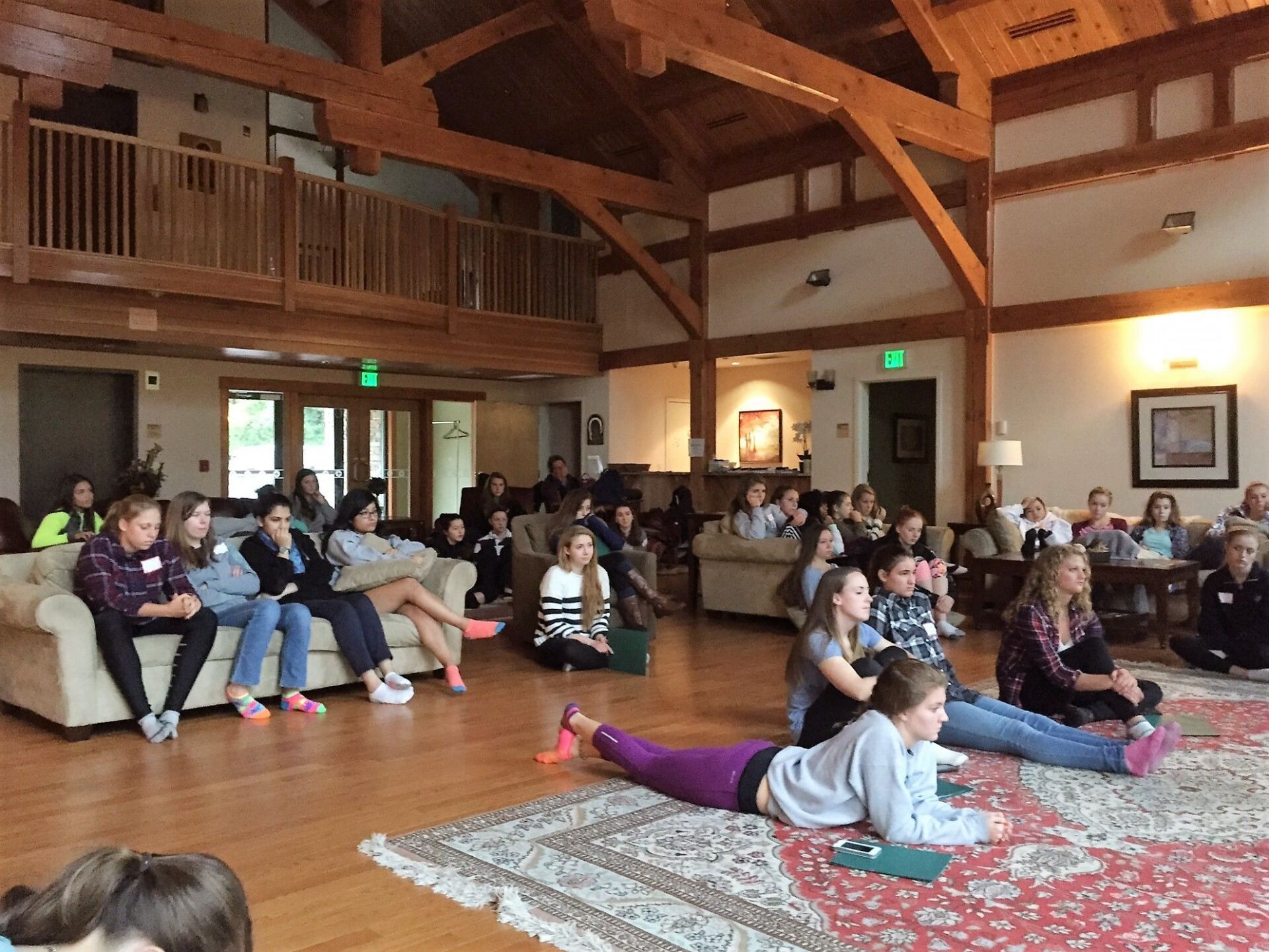 Group of students sitting on couches and the floor inside a building with wood beams. 