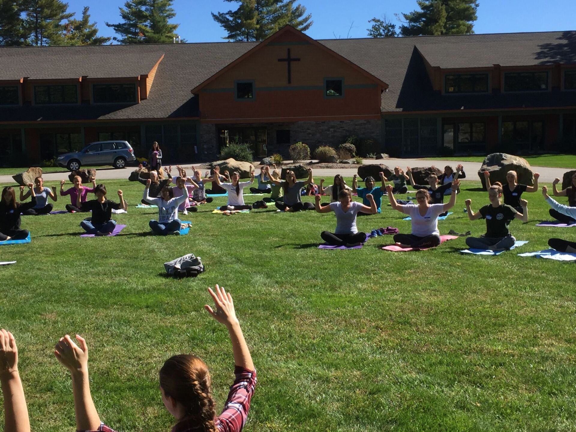 group of students outside with their arms up while sitting on mats on the grass 
