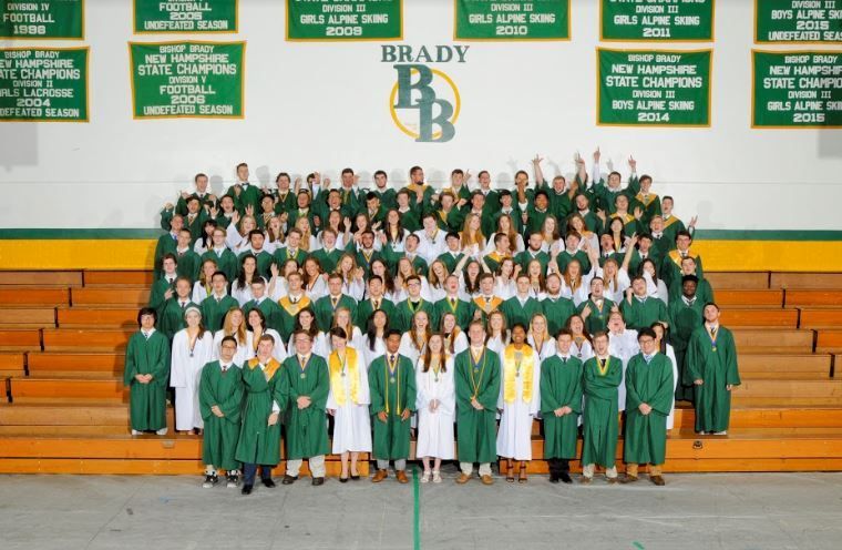image of graduating class in cap and gowns standing on bleachers in gym