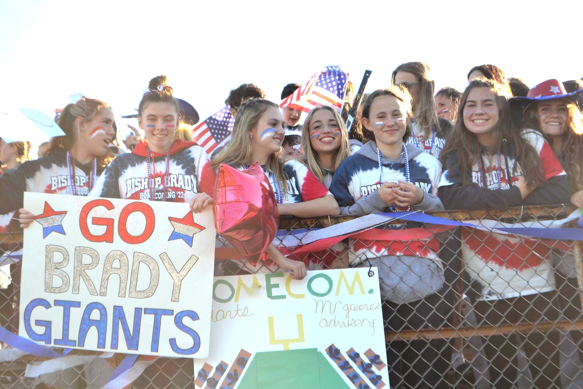 image of students wearing red, white in blue on bleachers outside holding sings 