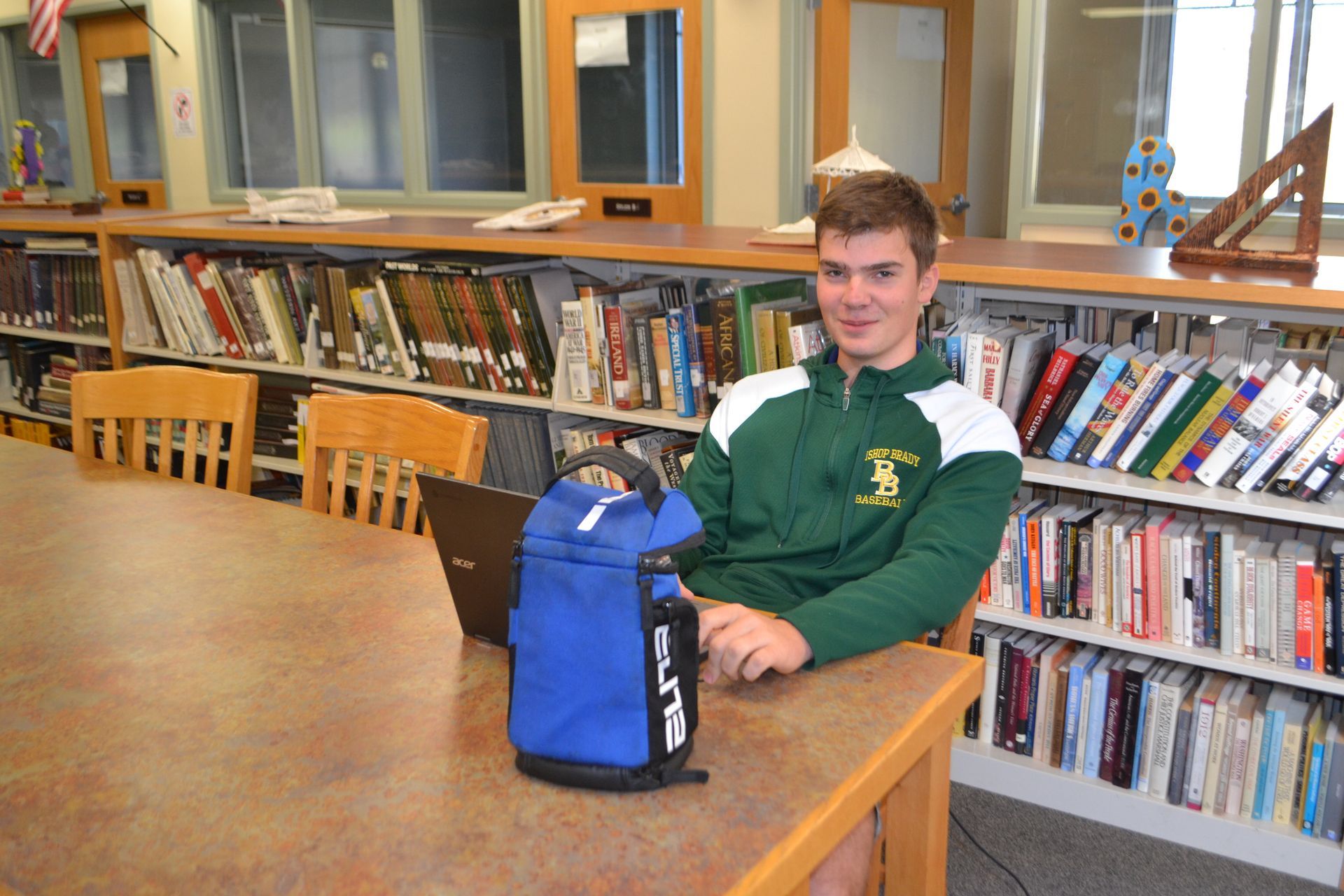 student sitting at a table in the library with bookcases behind him.