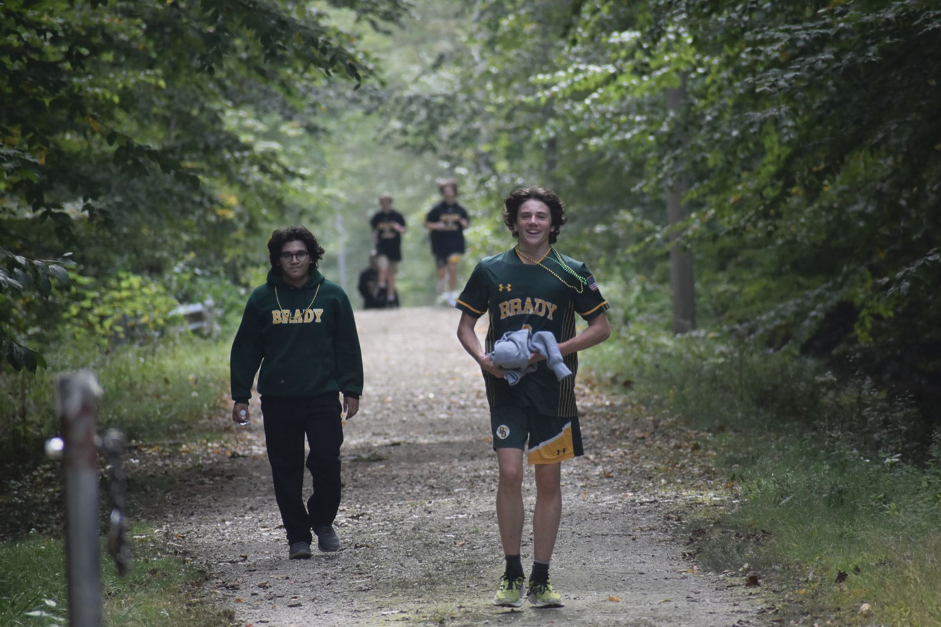 2 students walking on a trail with trees on the side of trail