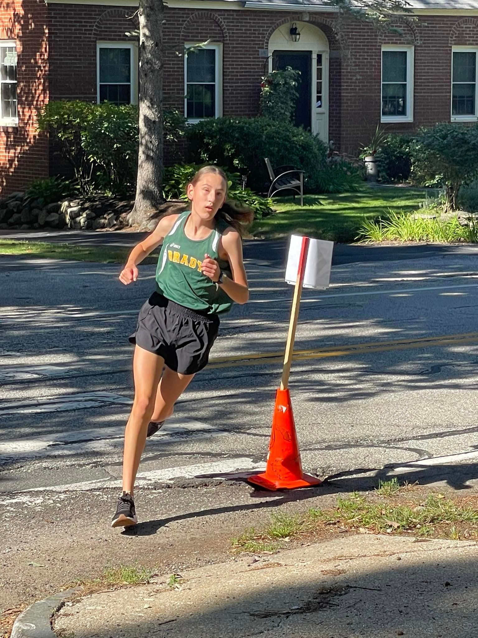 image of female runner in brady shirt with street and house behind her, 