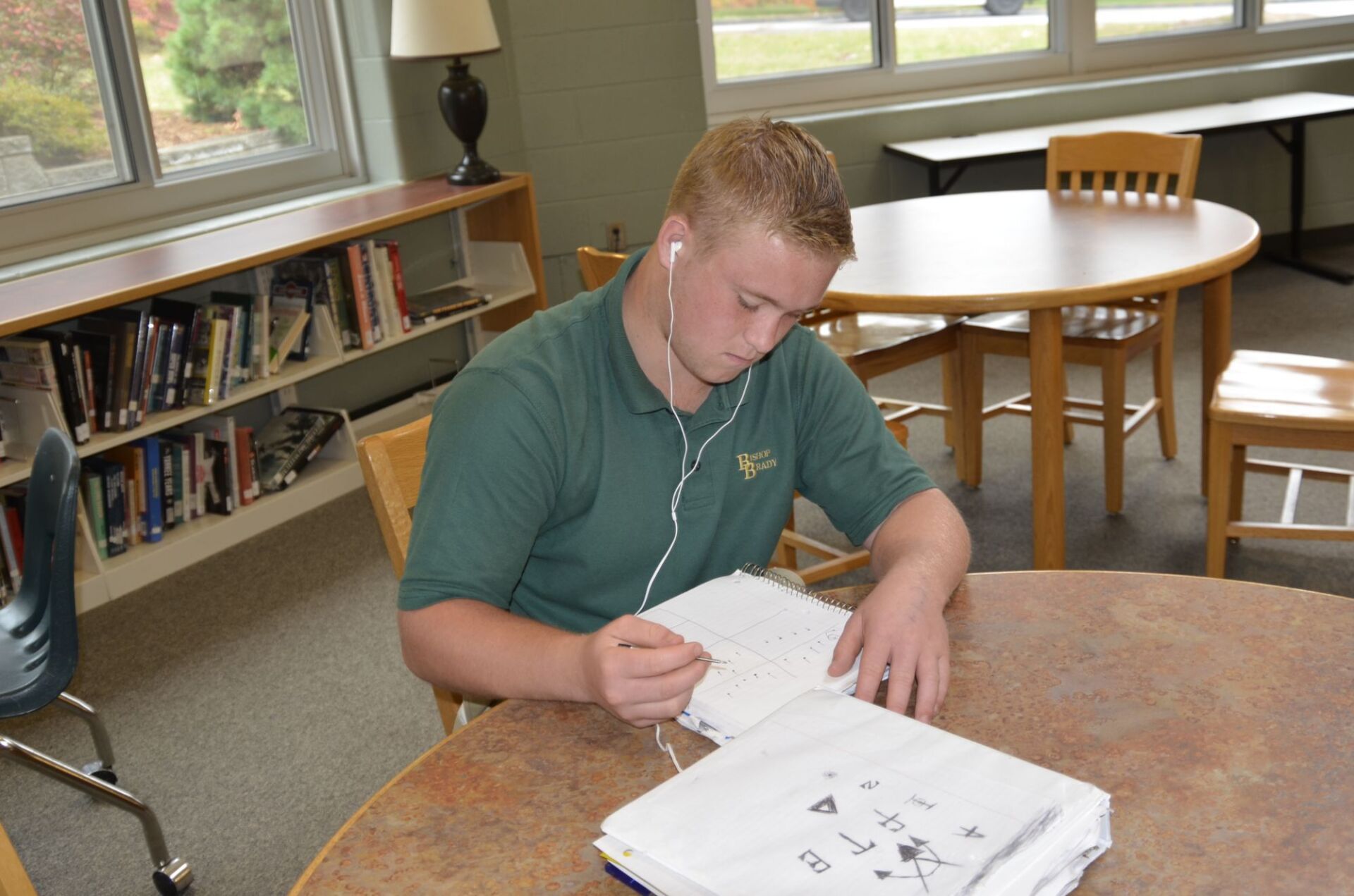 male student writing in a notebook at a round table in the library.