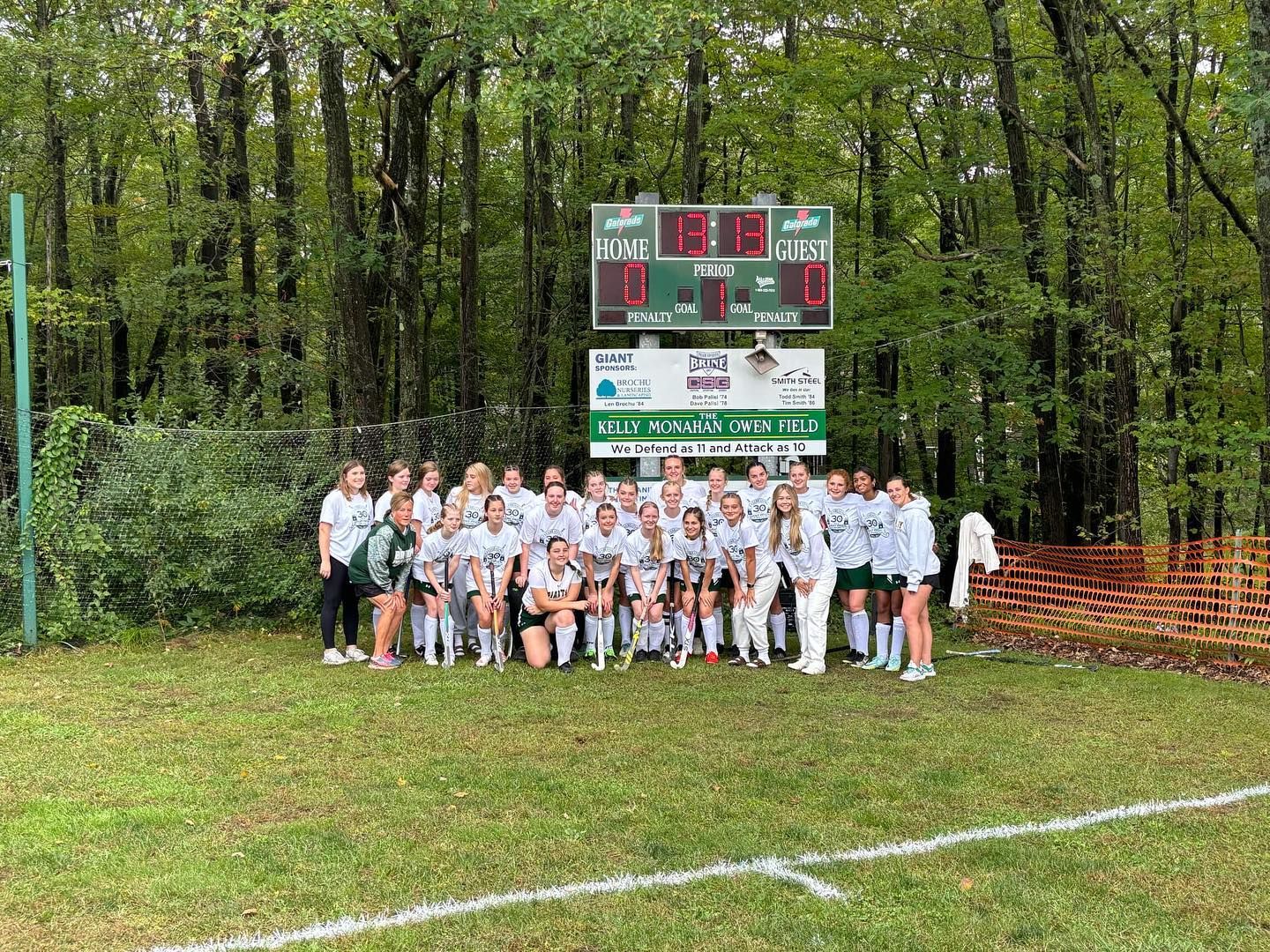 field hockey team in front of score board and trees in background