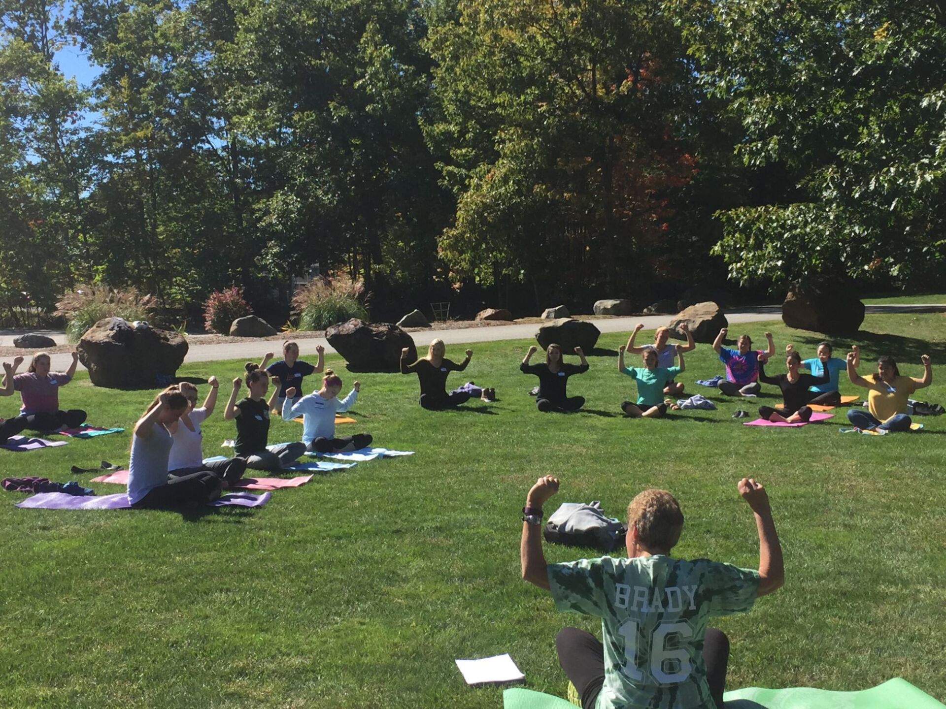 group of students outside with their arms up while sitting on mats on the grass 