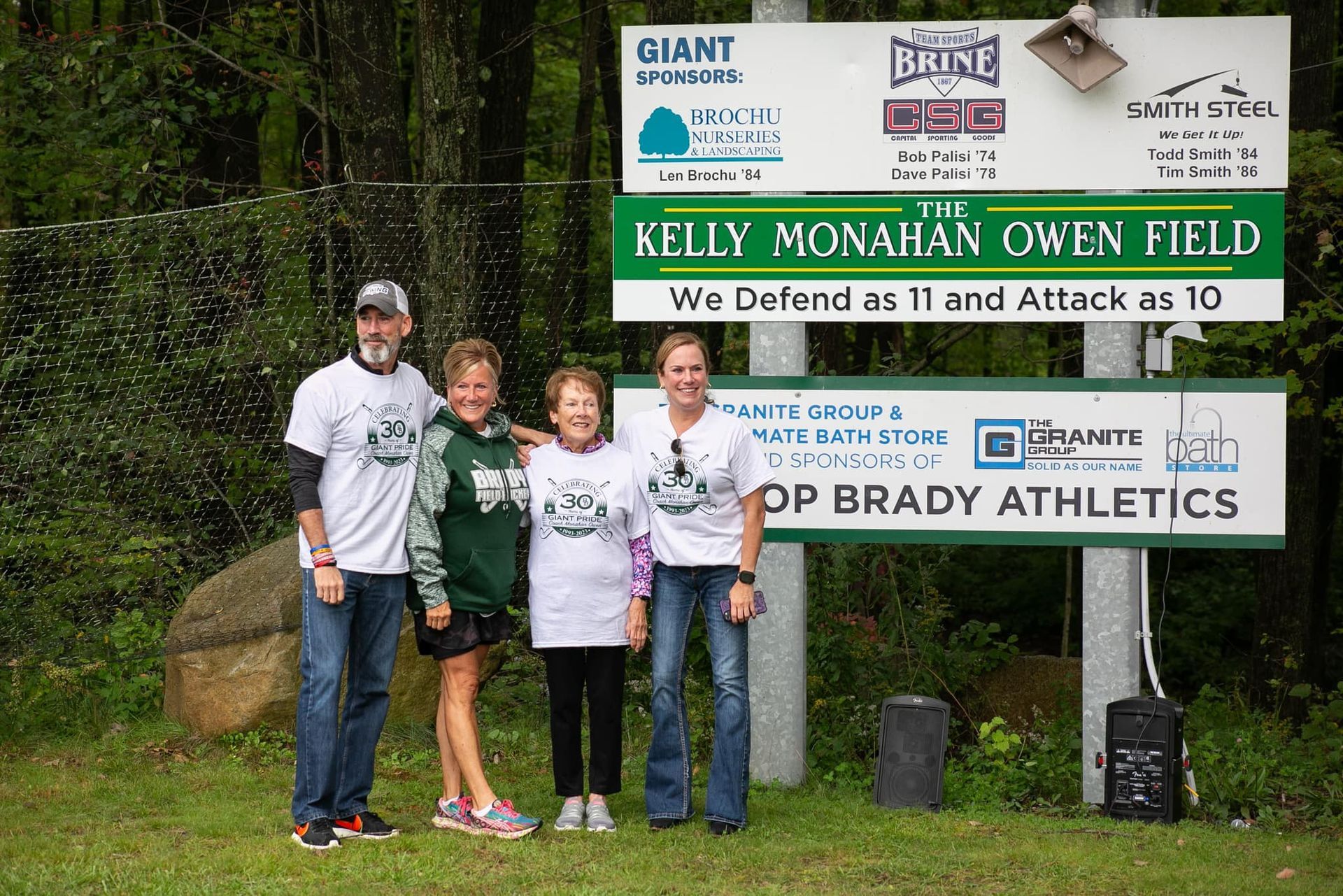 Field hockey coach with her husband and parents in front of the sign at the Kelly Monahan Owen Field. 