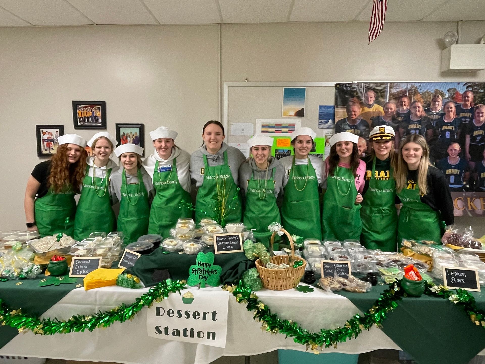 group of students in green aprons with table of baked good in front of them